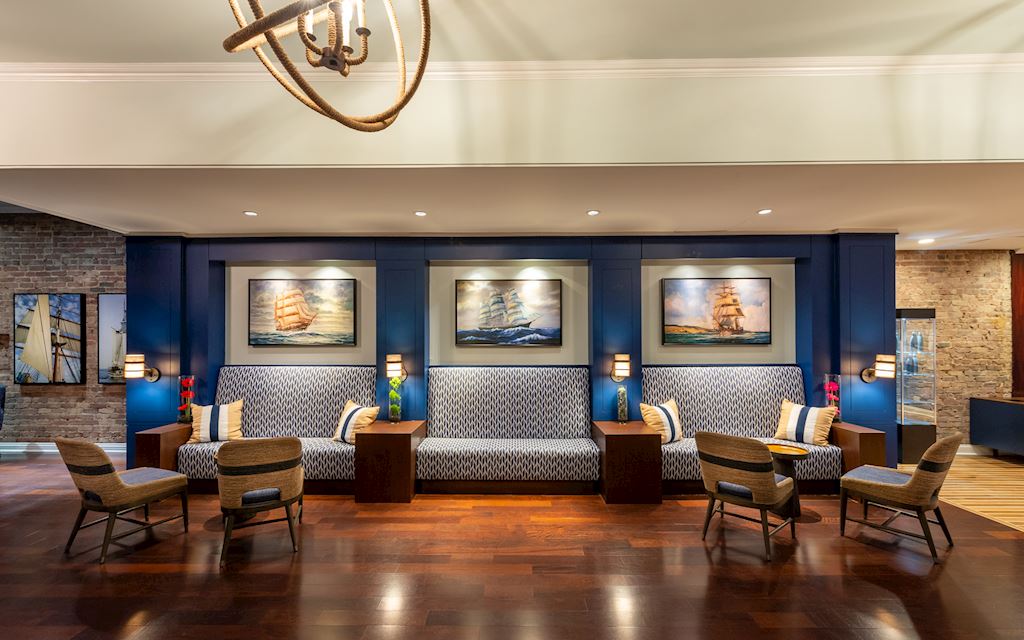 Lobby space with chairs, plush benches, and paintings of ships on the walls